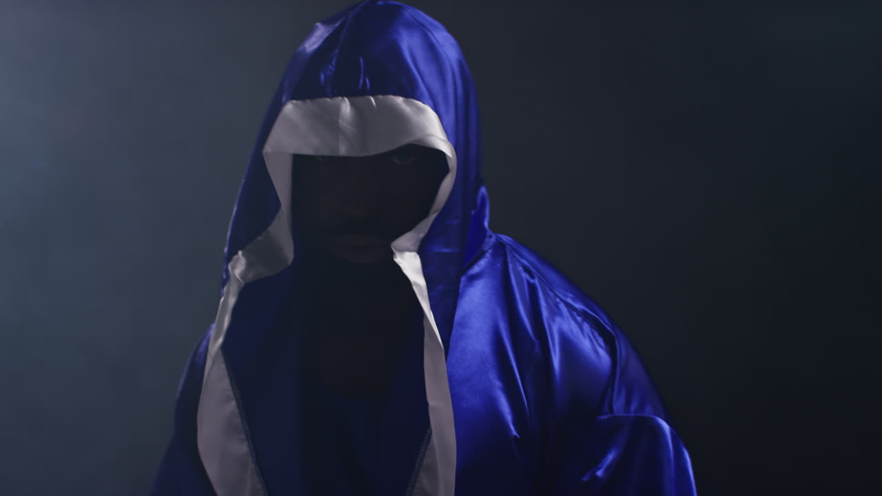 портрет боксера в халате, входящего в ринг в начале боксерского матча, бьющегося в перчатки вместе с низким ключевым освещением