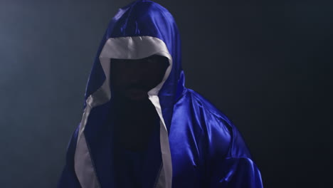 portrait of boxer wearing robe entering ring at start of boxing match hitting gloves together with low key lighting