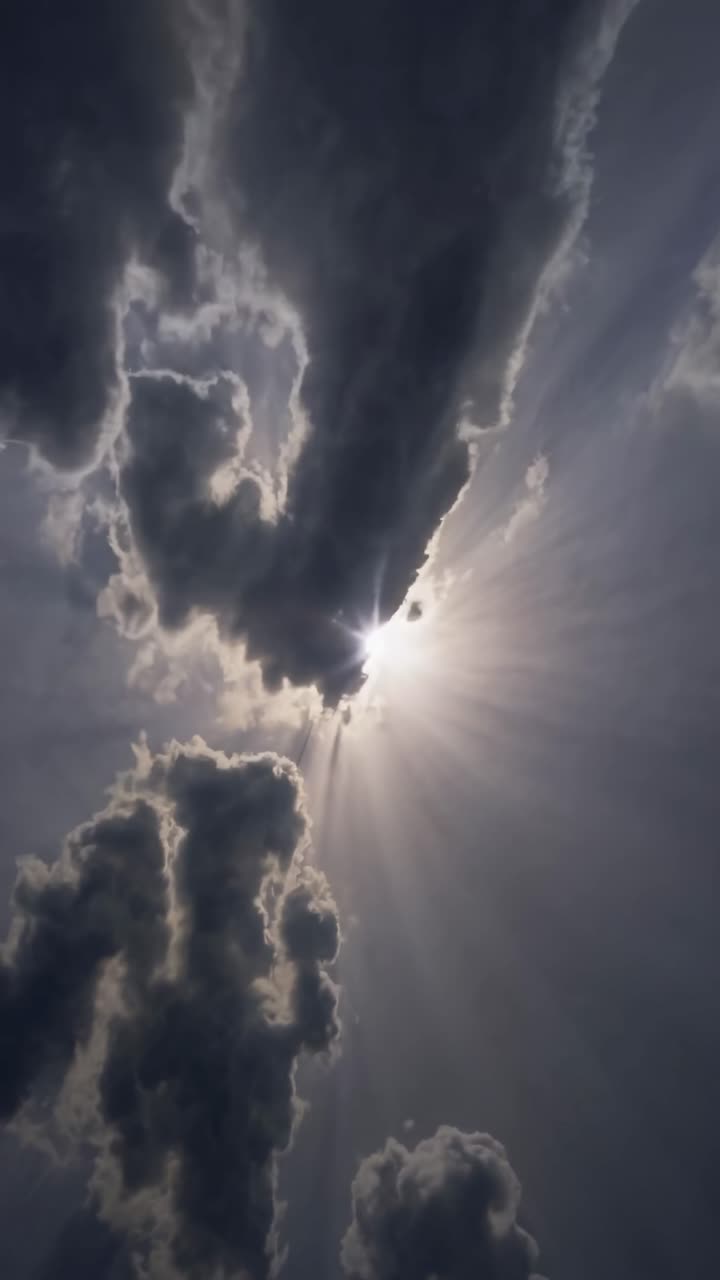 Angolazione drammatica dal basso verso l'alto che cattura i raggi solari che filtrano tra nuvole scure, creando un effetto cinematografico.
