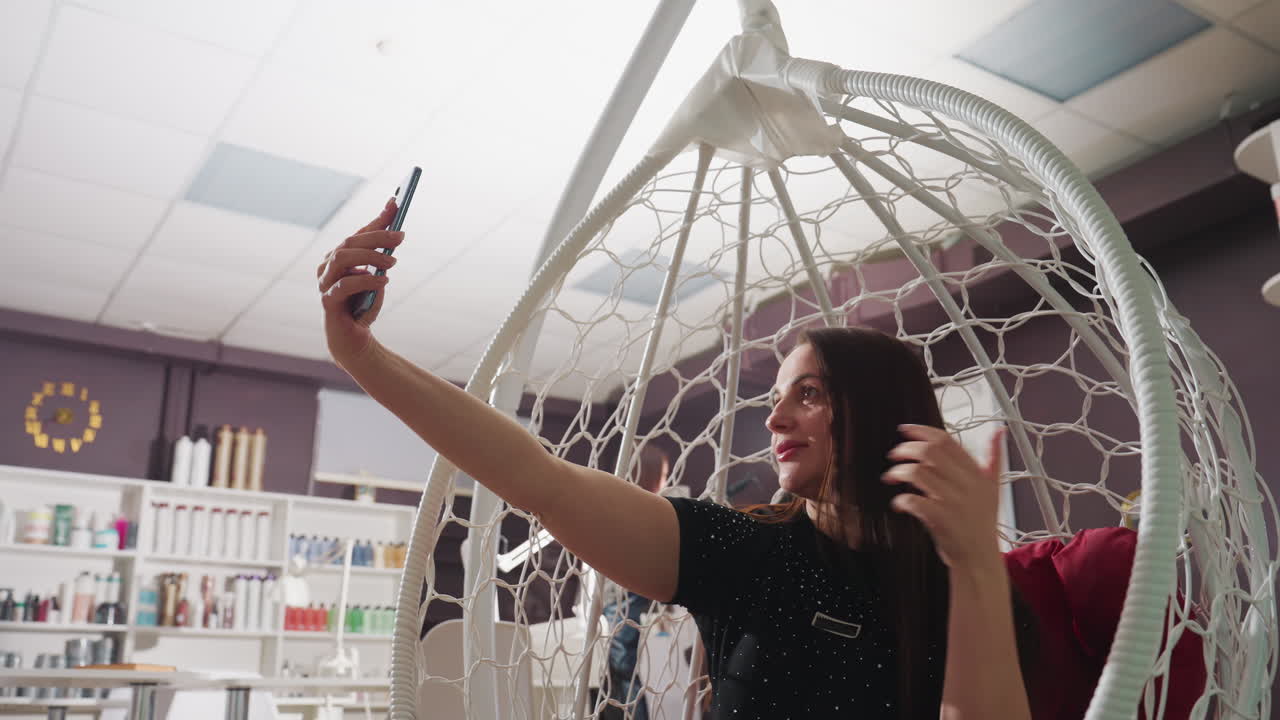 Kvinne i salong poserer selvsikkert med produkter, sjarmerende kvinne inntar en selvsikker positur med salongprodukter og belysning, avslappet bilde av kvinne som kaster på håret mens hun tar selfie i salongmiljø