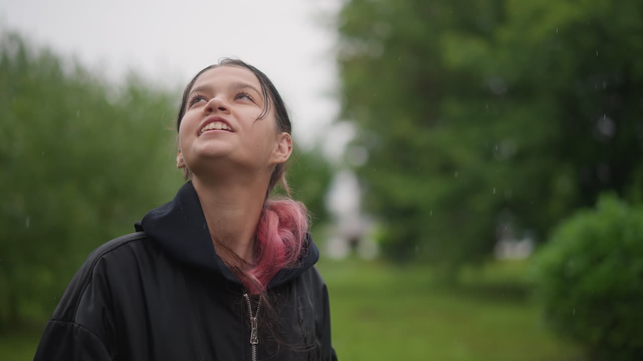 Retrato íntimo de mulher sob chuva suave. Menina com cabelo trançado sorrindo suavemente em tempo chuvoso. Mulher com trança com pontas rosadas olhando para cima com expressão serena durante uma garoa leve.