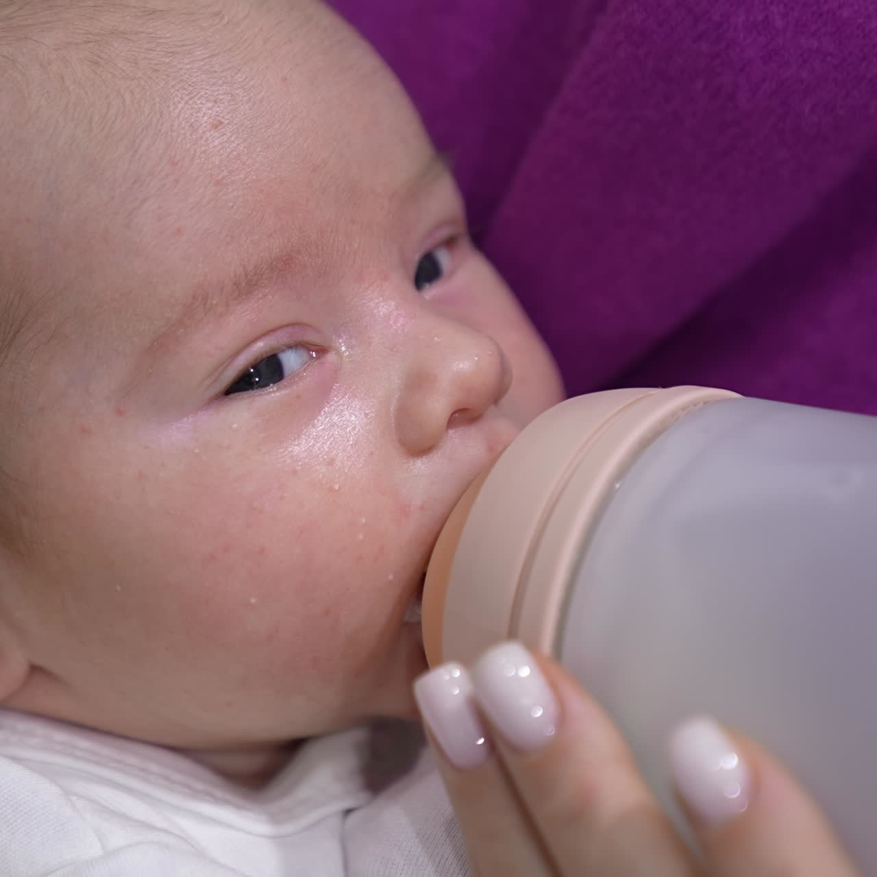 Baby being fed with milk from a bottle. Lovely child is suckling milk and moving his eyes right and left. Close up portrait