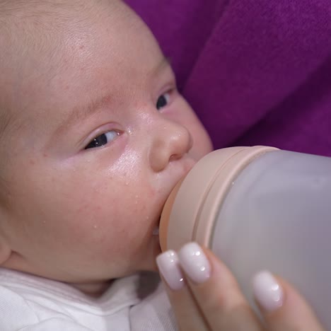 baby being fed with milk from a bottle. lovely child is suckling milk and moving his eyes right and left. close up portrait