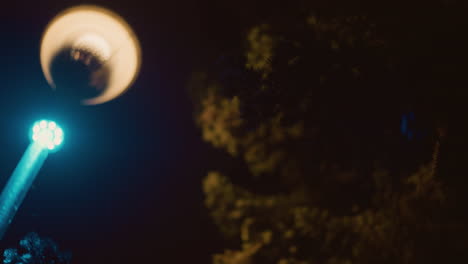 close-up view of a brightly illuminated street light at night, casting a blue glow with the silhouette of a tree in the background