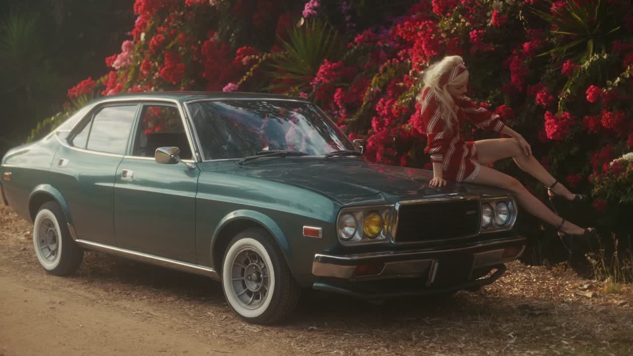 Mujer rubia con estilo posando en el capó de un coche verde clásico