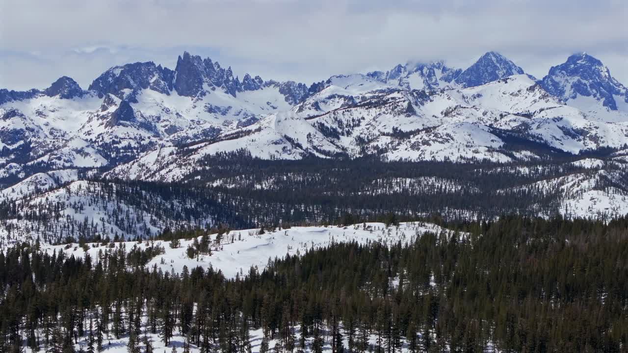 Minarets jagged towering peaks vista point panoramic landscape Mammoth Mountain ski resort aerial drone California winter spring sunny blue sky morning clouds Hemlocks Inyo National Forest forward pan