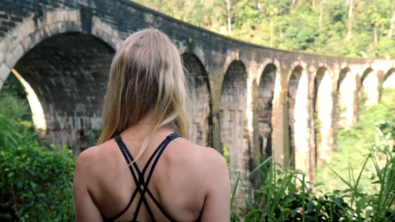A young woman observes the historic Nine Arch Bridge from a nearby hillside in Ella, Sri Lanka.