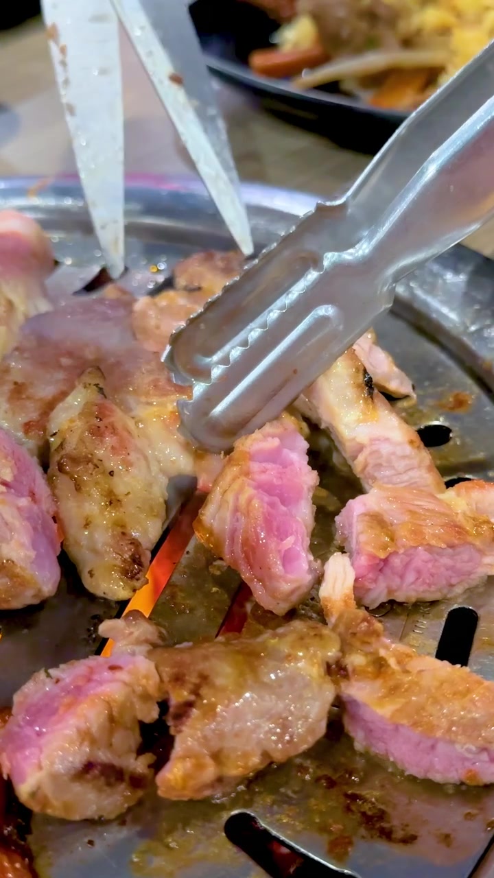 Tampilan dekat daging BBQ Korea mendesis di atas panggangan di restoran Bangkok, menonjolkan tekstur berair dan warna cerah