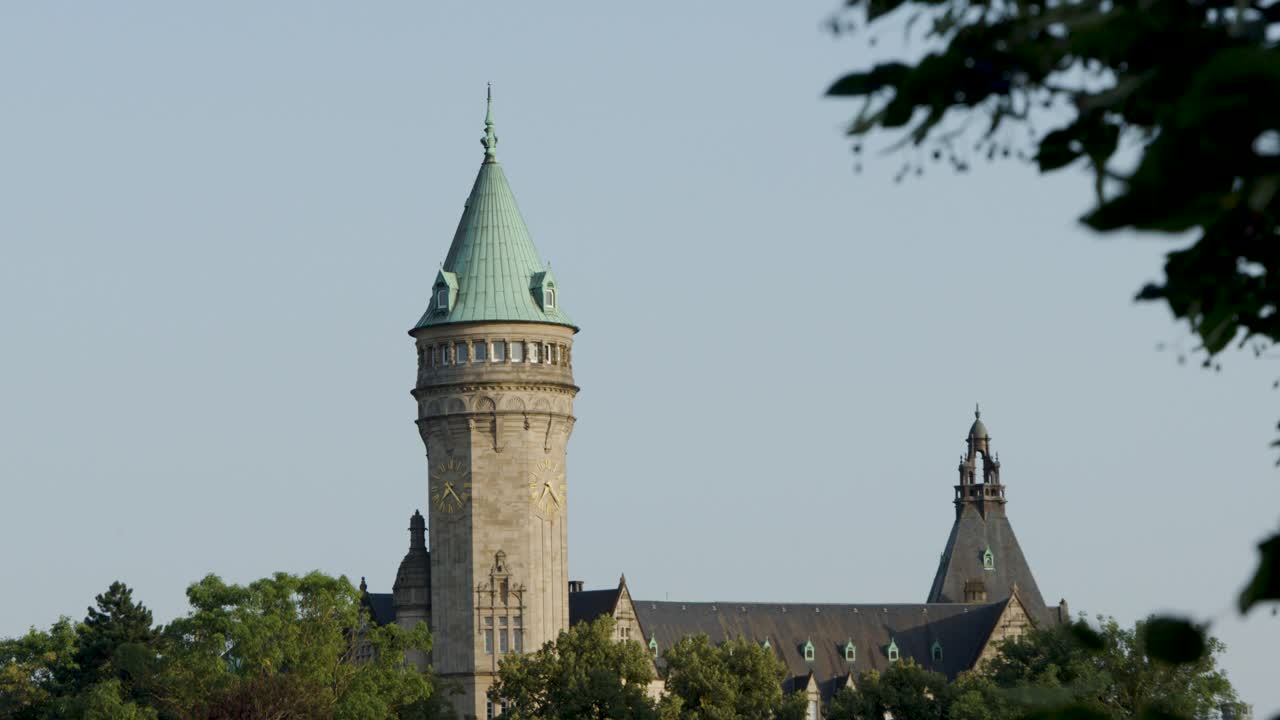 Daytime camera pan reveals stone tower, green trees, and blue sky in Luxembourg