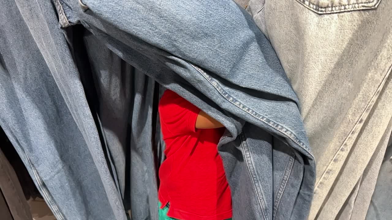 재미있고 사랑스러운 2살 아프로 유럽 어린이가 엄마와 함께 가게 안에서 숨바꼭질을 하고 있습니다.