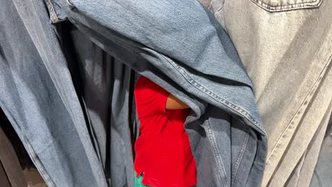 funny and lovely two year old afro european child playing hide-and-seek inside a shop wth mum