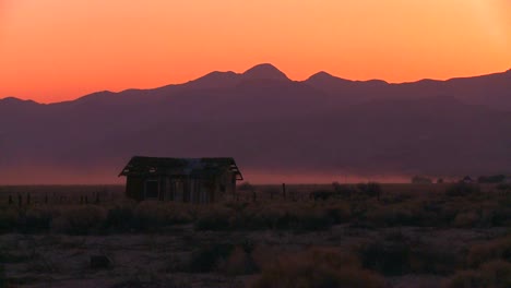 the sun sets behind an abandoned cabin the desert