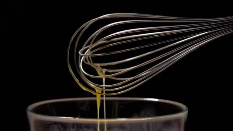 medium shot of a whisk with dropping beaten eggs in slow motion