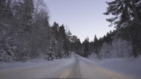 pov of car driving on snowy road in winter forest