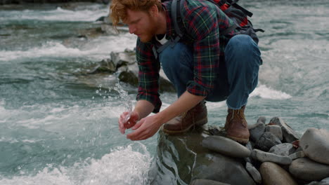 Tourist-sitting-on-rock-at-river-bank.-Man-washing-hands-in-mountain-stream