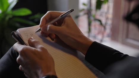 close view of artist and writer, with legs crossed, writes new lyrics for music or books in a notebook