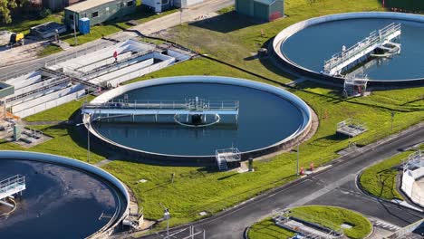 rotating camera captures circular water treatment tanks, industrial structures, and a worker at a modern sewage facility under bright daylight in gold coast, australia