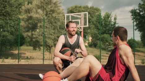 Zwei-Männliche-Basketballspieler-Machen-Eine-Pause-Und-Unterhalten-Sich-Während-Ihrer-Trainingseinheit-Auf-Einem-Basketballplatz-Im-Freien