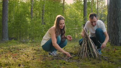 A-smiling-woman-and-man-together-in-the-woods-collect-and-set-up-campfire-sticks-at-sunset-during-a-family-camping-trip