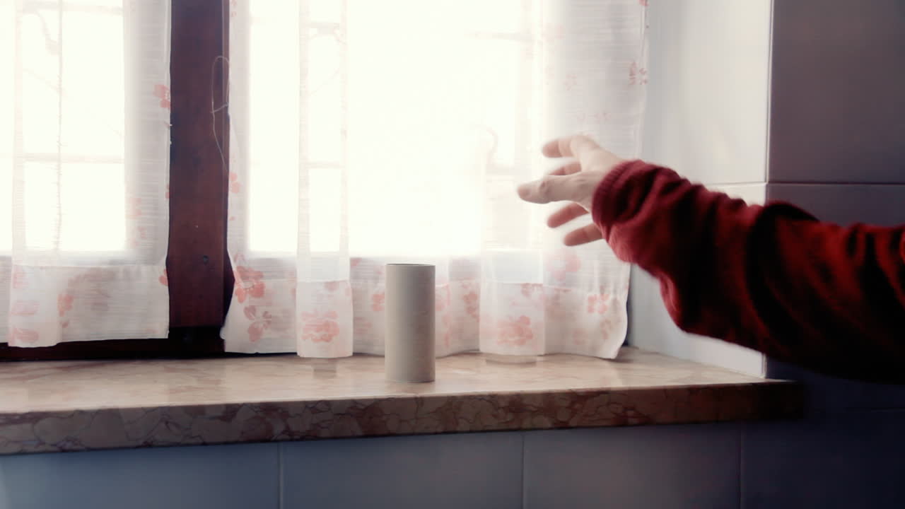 A man in the bathroom, reaching for the toilet paper roll, discovering that there's no more of it, reacting with anger