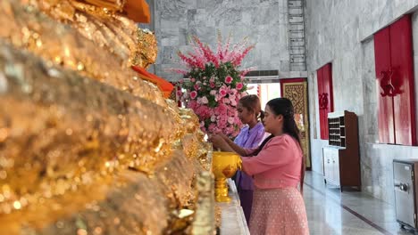 women offering gold leaf at a thai temple