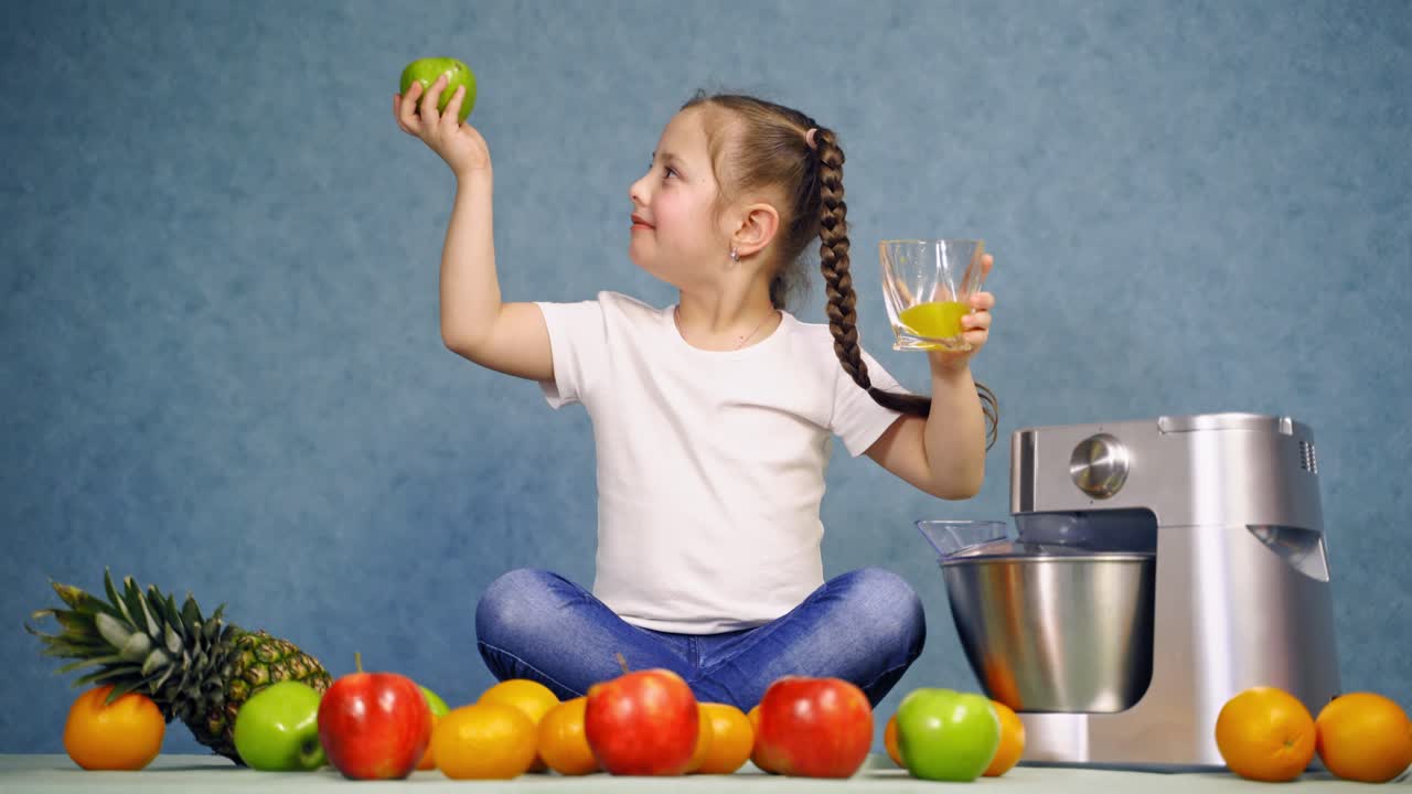 Girl with glass of orange juice. Little girl eating apple with homemade juice