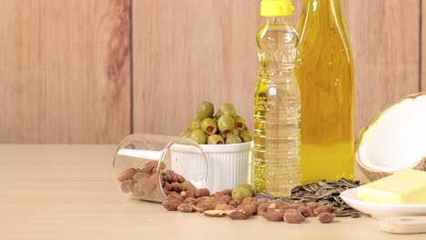 a variety of high-fat foods including avocado, coconut, bacon, butter, nuts, oil, and olives arranged on a wooden table, captured in bright studio lighting with a smooth left-to-right pan