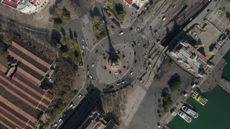 aerial: overhead shot of columbus monument roundabout in barcelona, spain with busy car traffic on sunny day [4k]