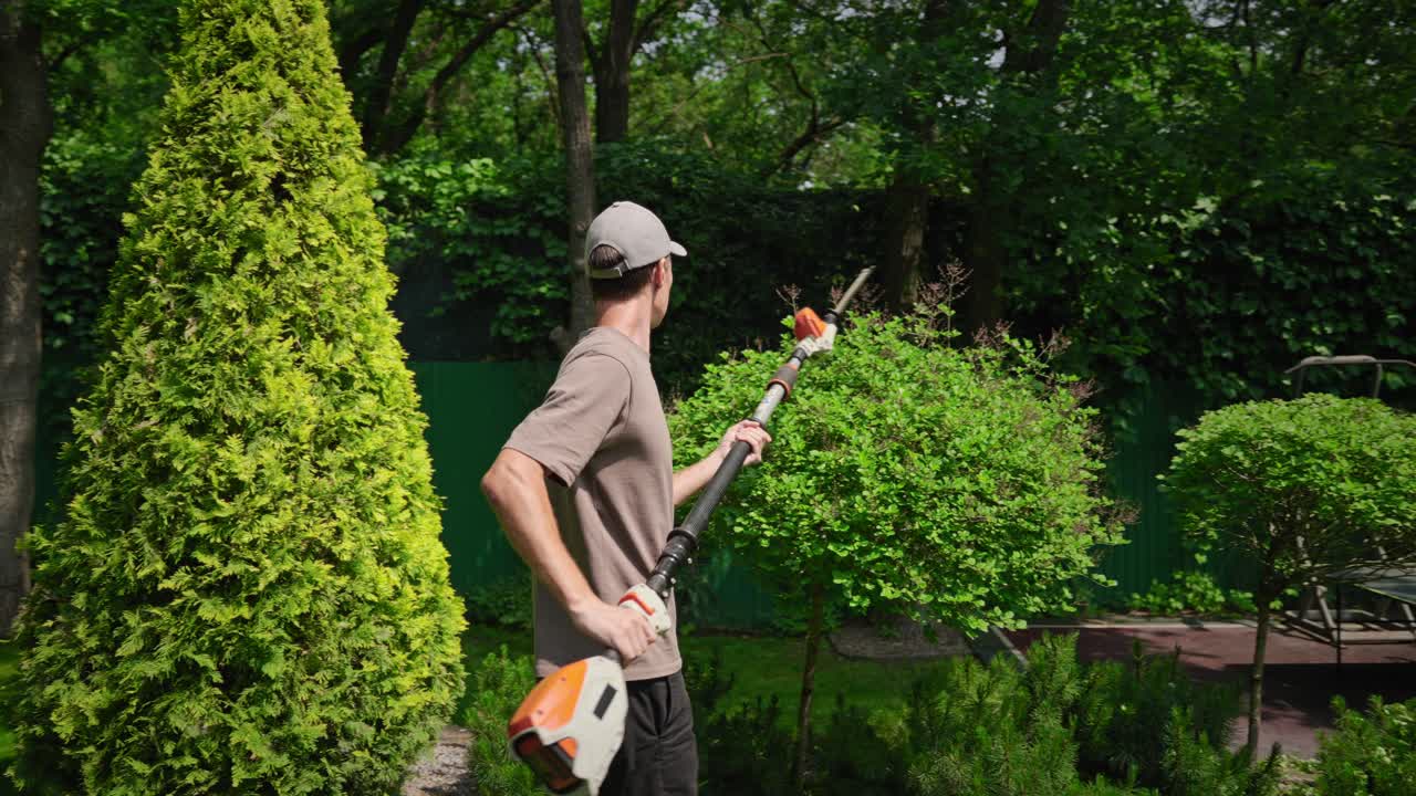 Man Trimming Bushes in a Green Garden with a Hedge Trimmer