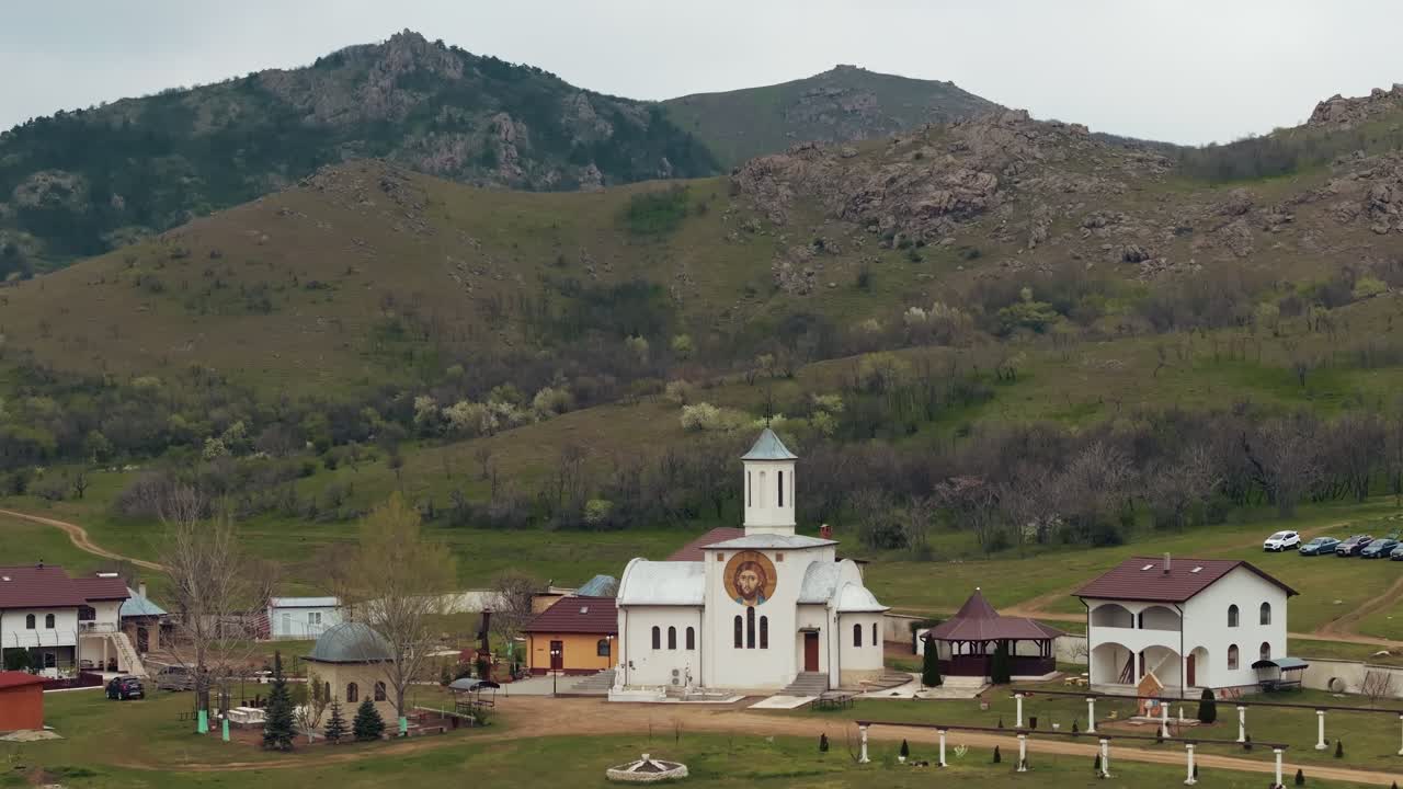 Complesso monastico rurale e sereno annidato alla base di dolci colline verdi e montagne rocciose.