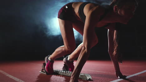 atleta femenina en un fondo oscuro se está preparando para correr el sprint de cross-country desde las almohadillas en la cinta de correr en un fondo oscuro