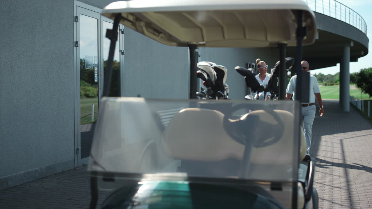 부유한 커플이 골프 코스를 걸어서 골프 카트를 운전합니다. 스포츠 팀은 컨트리 클럽을 즐 ⁇ 니다.