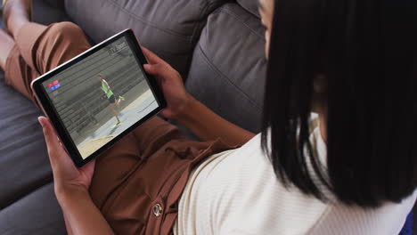 compuesto de una mujer sentada en casa en el sofá viendo un evento de salto de longitud de atletismo en una tableta