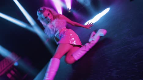 Camera-energetically-orbits-around-a-dancing-girl,-mirroring-her-movements,-unfolding-on-a-stage-with-pink-lighting