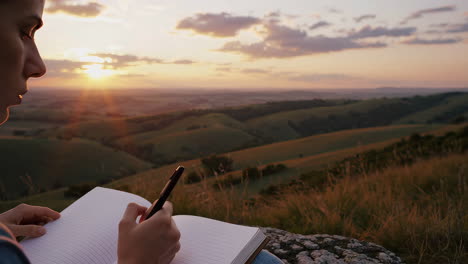 person writing in notebook at sunset overlooking scenic landscape
