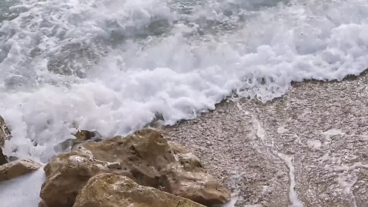Onde oceaniche che si infrangono con forza sulle grandi rocce costiere, creando acqua bianca, schiuma e un movimento turbolento, mostrando la pura energia marina e l'interazione naturale con la costa alla luce del giorno.