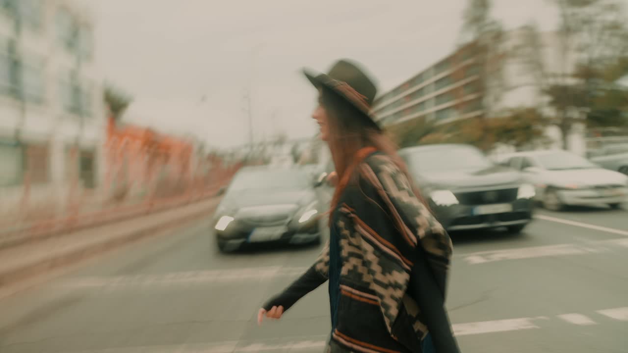 Young Woman in Hat and Poncho Walking Across City Street