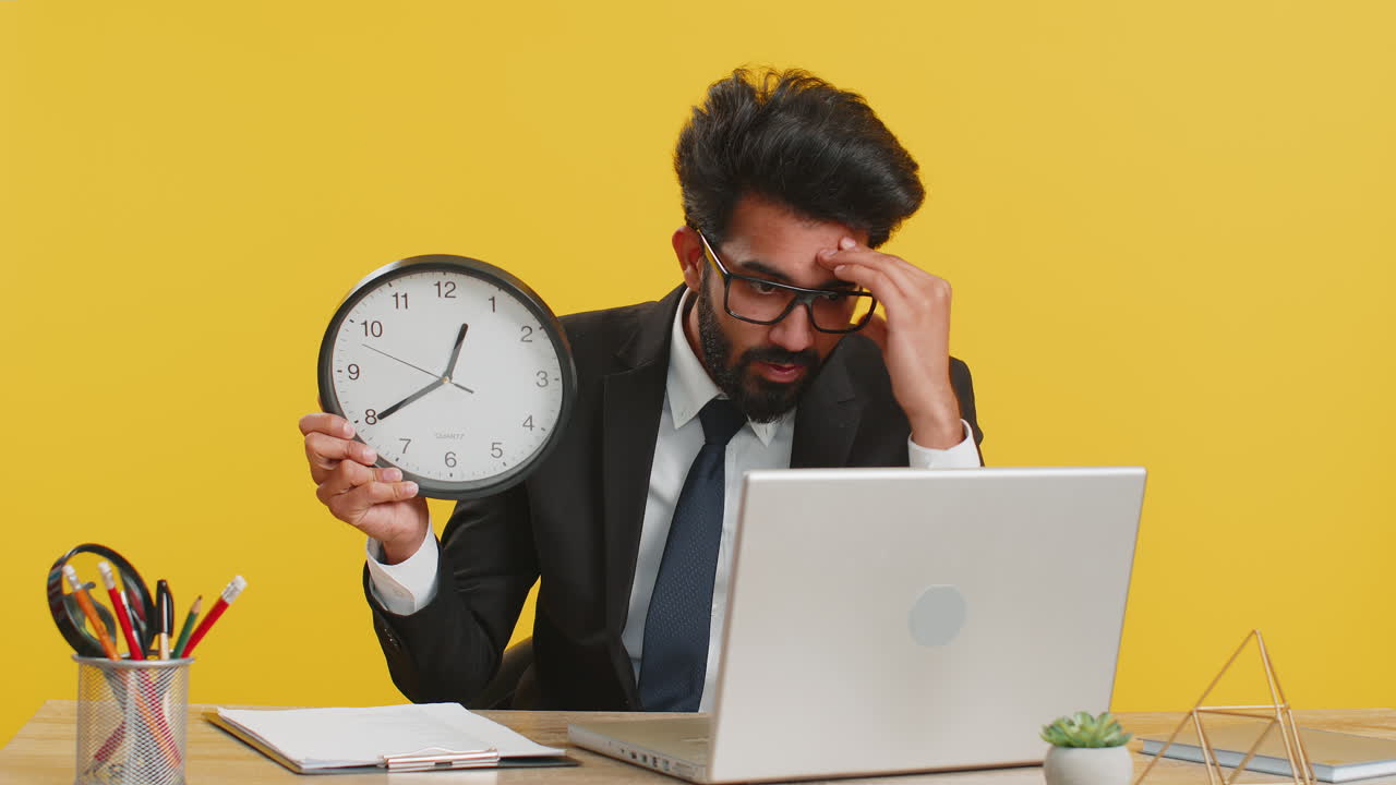 Indian business man with anxiety checking time on clock running late to work being in delay deadline