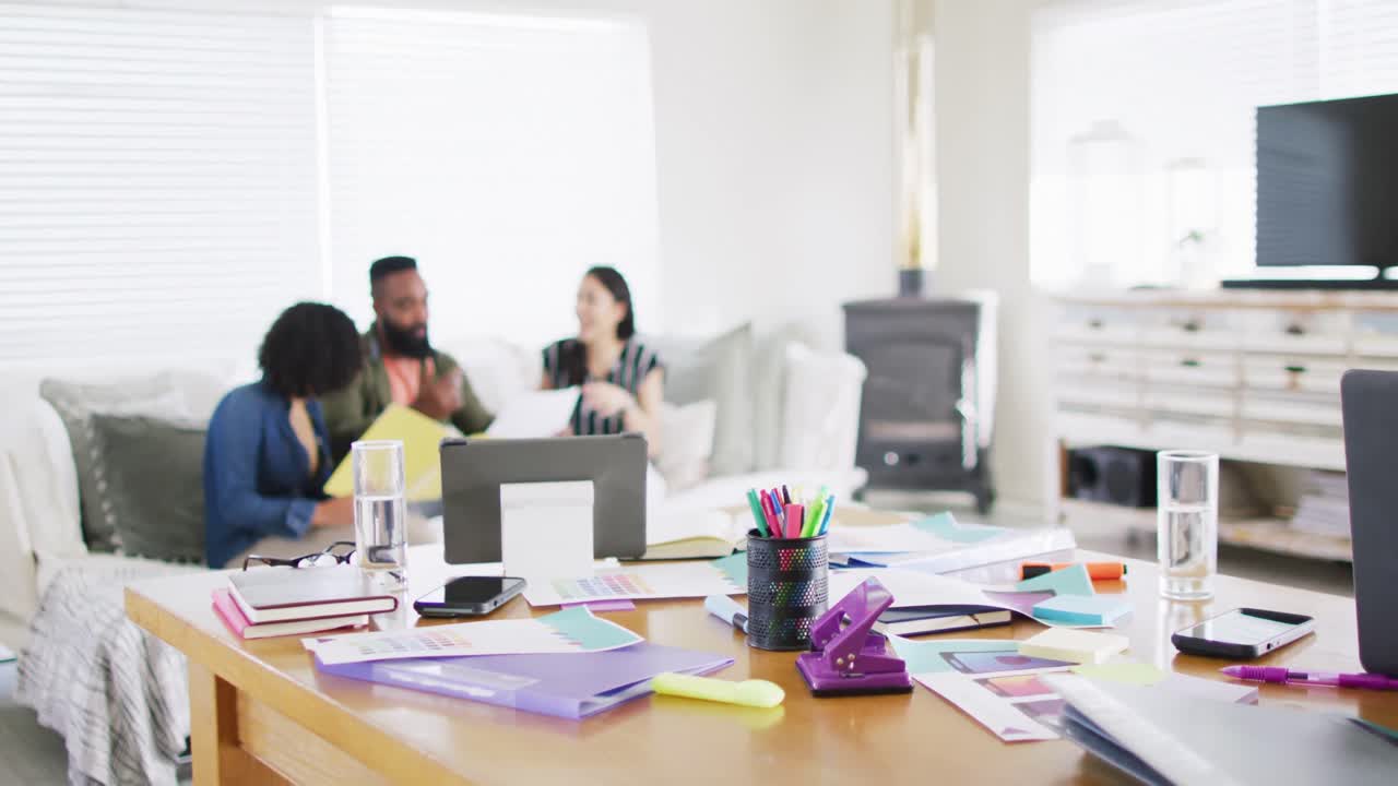 Busy desk and diverse friends working together on couch in background, in slow motion