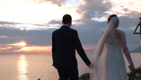 bride and groom walking near the sea at sunset