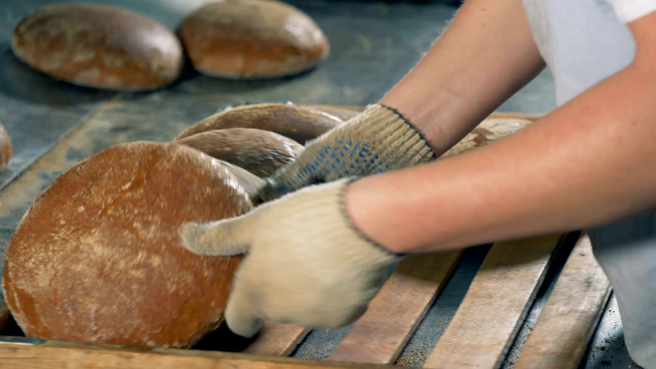 un trabajador recoge panes redondos calientes en una bandeja de madera para empacar.