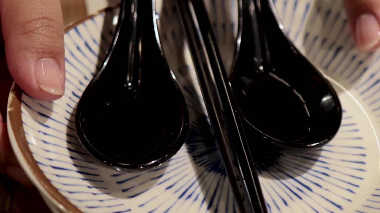 Close-up of hands arranging black spoons and chopsticks on blue-patterned plates.