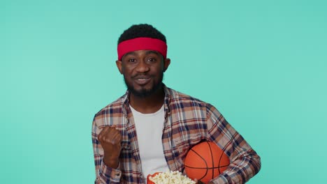 bearded african american young man basketball fan holding ball doing winner gesture, dancing alone