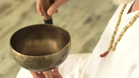 un homme âgé jouant au gong de bol avec un marteau