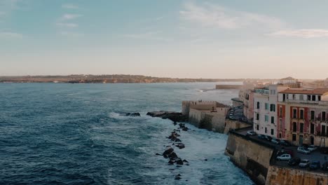 aerial drone shot of ortigia island along the mediterranean sea cost with large waves crashing on the fortress. historic charming medieval town in sicily at sunset.