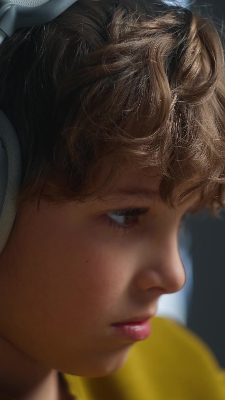 Bambino concentrato scrive con la matita e indossa le cuffie.
