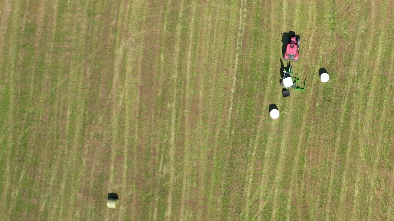 농장에서 흰색 플라스틱 클링 랩으로 둥근 건초 베일을 감싸는 농업용 트랙터