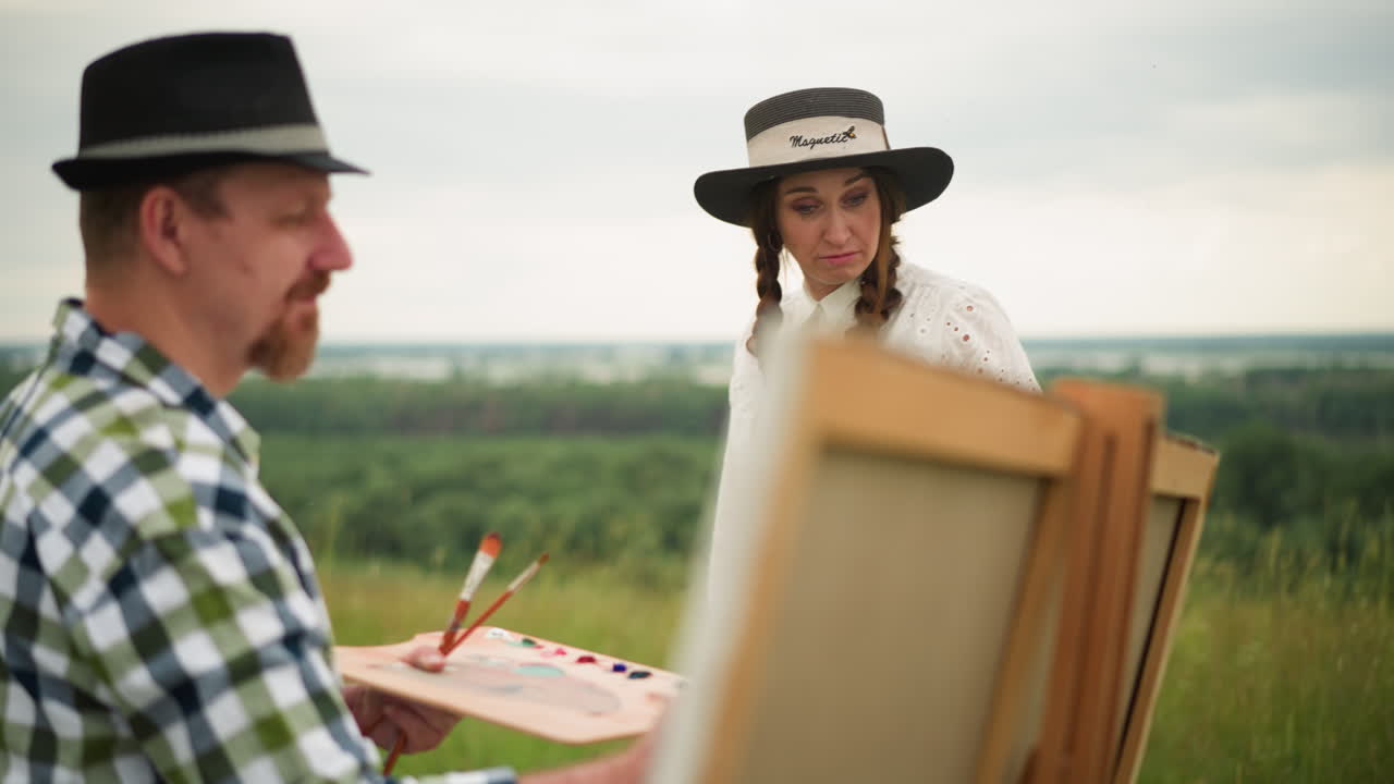 화가 한 명 은 야외 에서 큰 캔버스 에 작업 하는 동안 페인트 를 들고 있는 것 을 볼 수 있다. 그  에  드레스 와 모자 를 입은 한 여자 가 다가와, 걱정 이 나 불쾌 한 표정 을 보이고 있다.