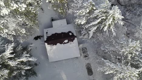 Cabin-Tucked-Away-in-Winter-Forest-Aerial-Rising-Reveal,-Top-Down