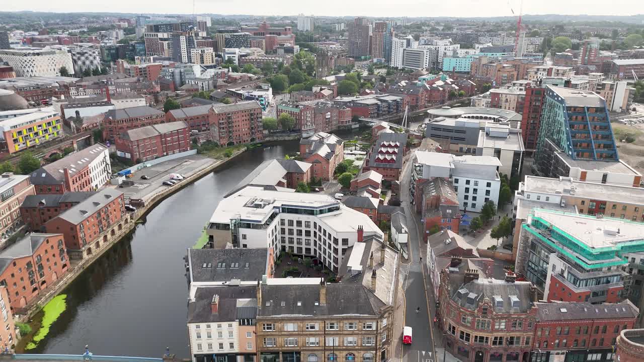 Drone footage pans above River Aire in Leeds, revealing Victorian buildings, modern architecture, and bridges under bright daylight with soft, even lighting